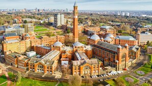 An aerial view of a university campus with historic buildings, a prominent clock tower, and surrounding green spaces.