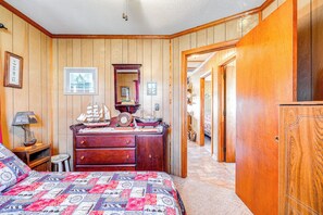 Ein Schlafzimmer mit einer holzgetäfelten Wand, einem Bett mit gemustertem Überwurf, einer Kommode mit einem Schiffsmodell und einem Spiegel.