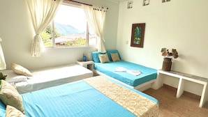A room with two beds, a desk, a window with curtains, a picture on the wall, and a vase with flowers.