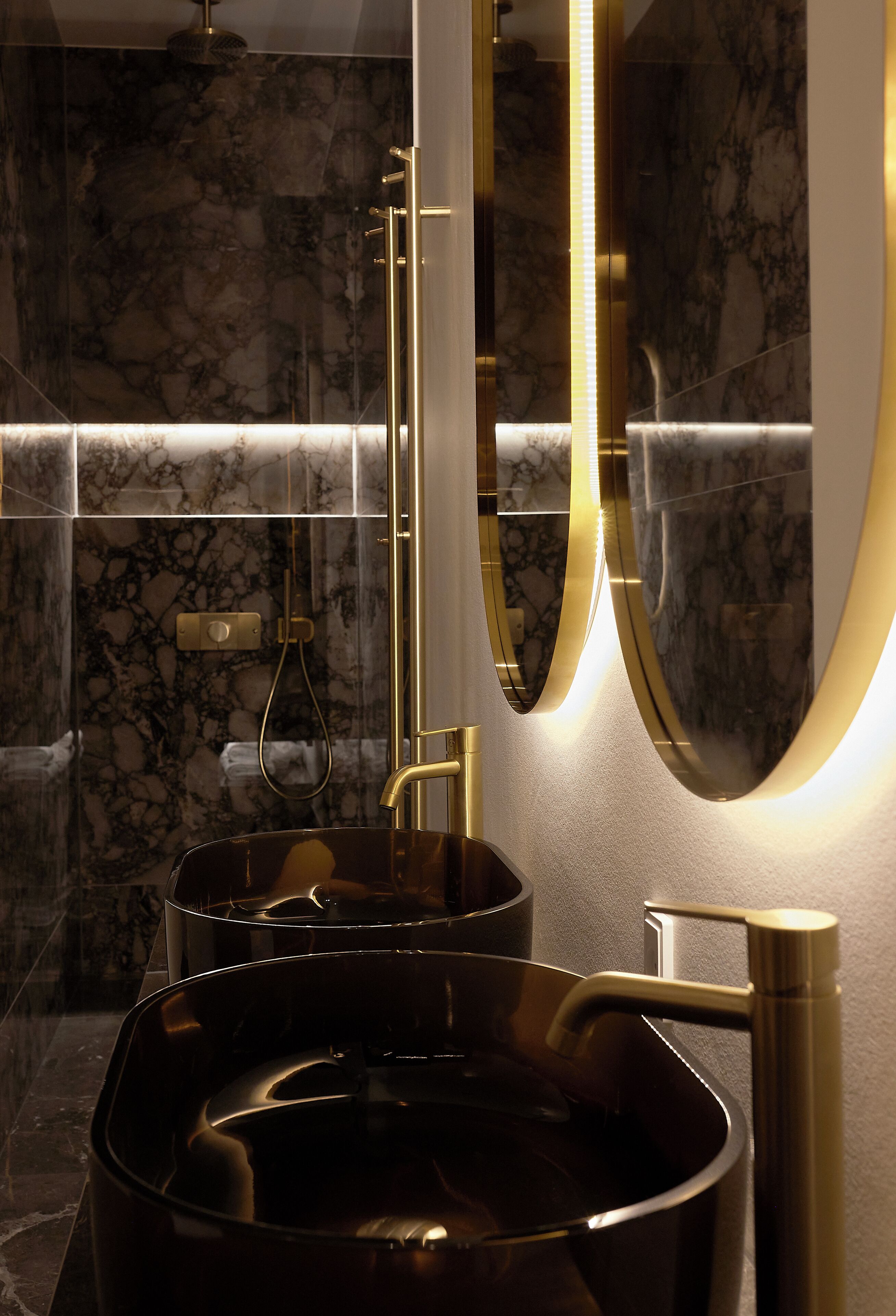 A modern bathroom with a marble wall, a large mirror, and a gold faucet.