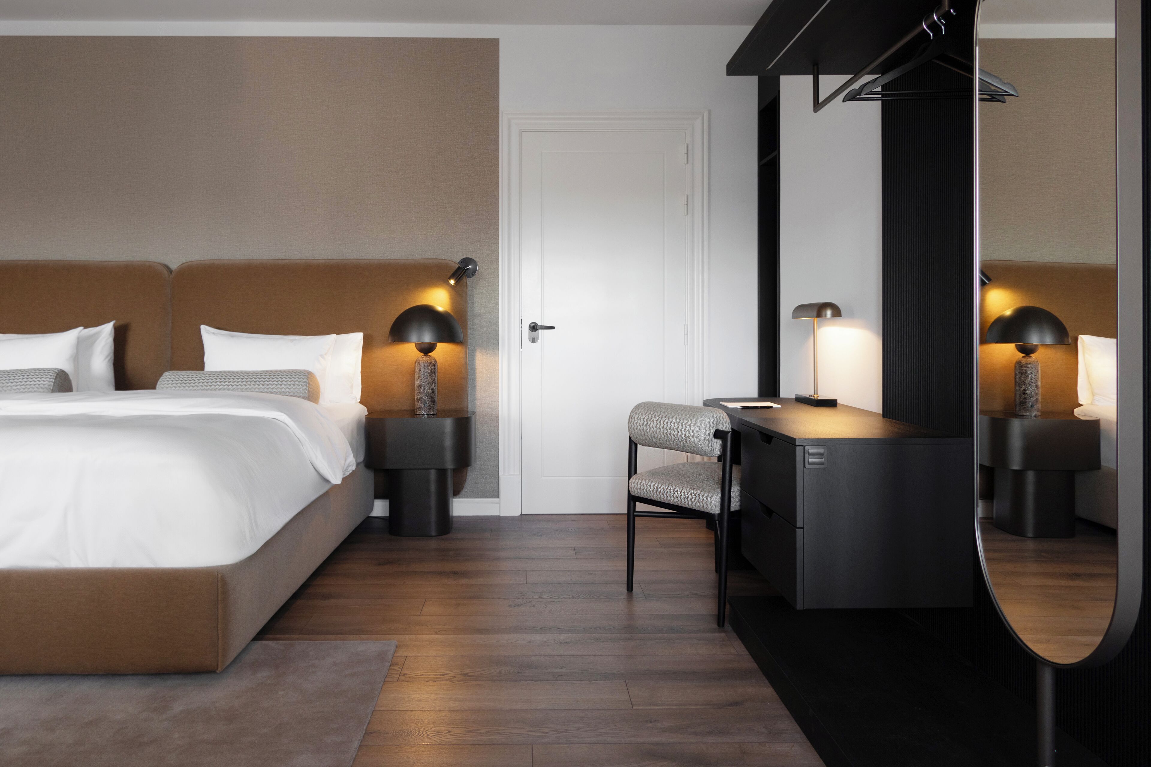 Una habitación de hotel moderna con una cama grande, mesitas de noche con lámparas, un escritorio y un espejo.