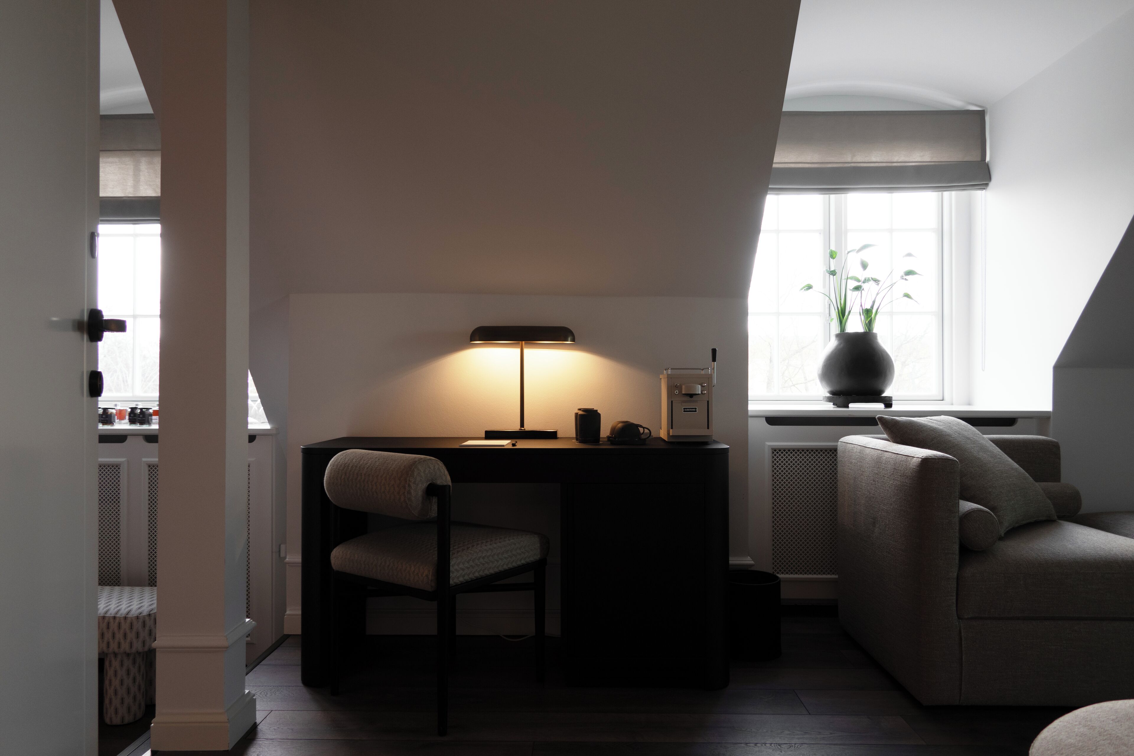A modern loft bedroom with a desk, chair, and a large window.