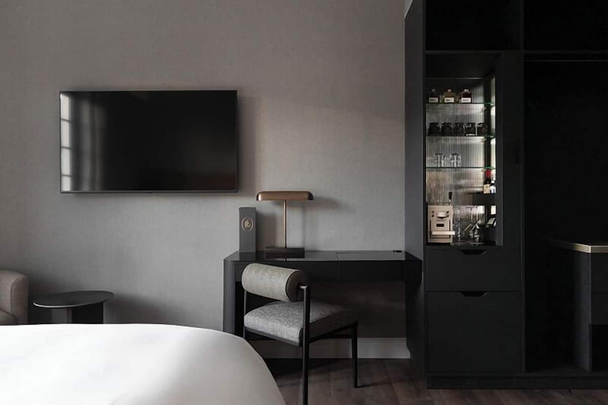 Una habitación de hotel moderna con una cama grande, un escritorio con una silla, un televisor de pantalla plana en la pared, una lámpara y un minibar.
