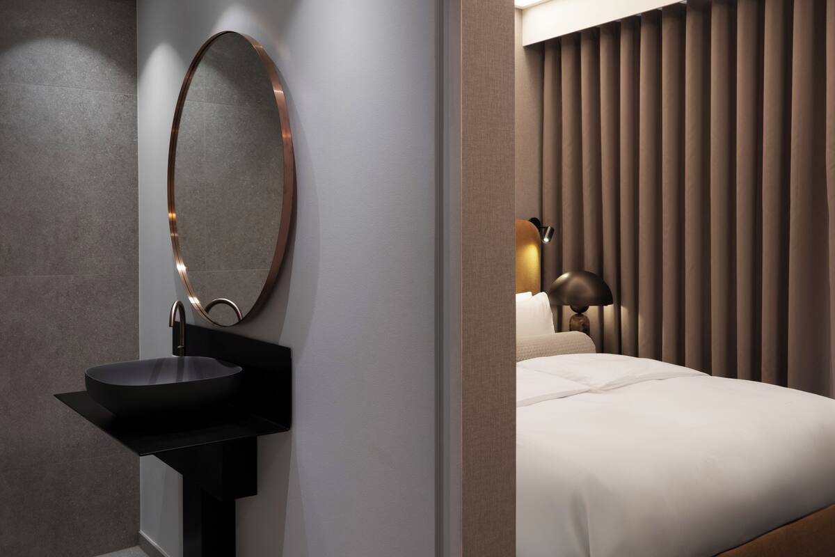 Un baño moderno con un espejo redondo, lavamanos negro y una lámpara de noche.