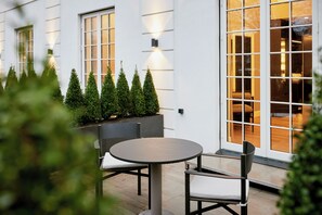 A patio with a round table and chairs, a planter with greenery, and a building with large windows and doors. - Park Lane Copenhagen (Hellerup)