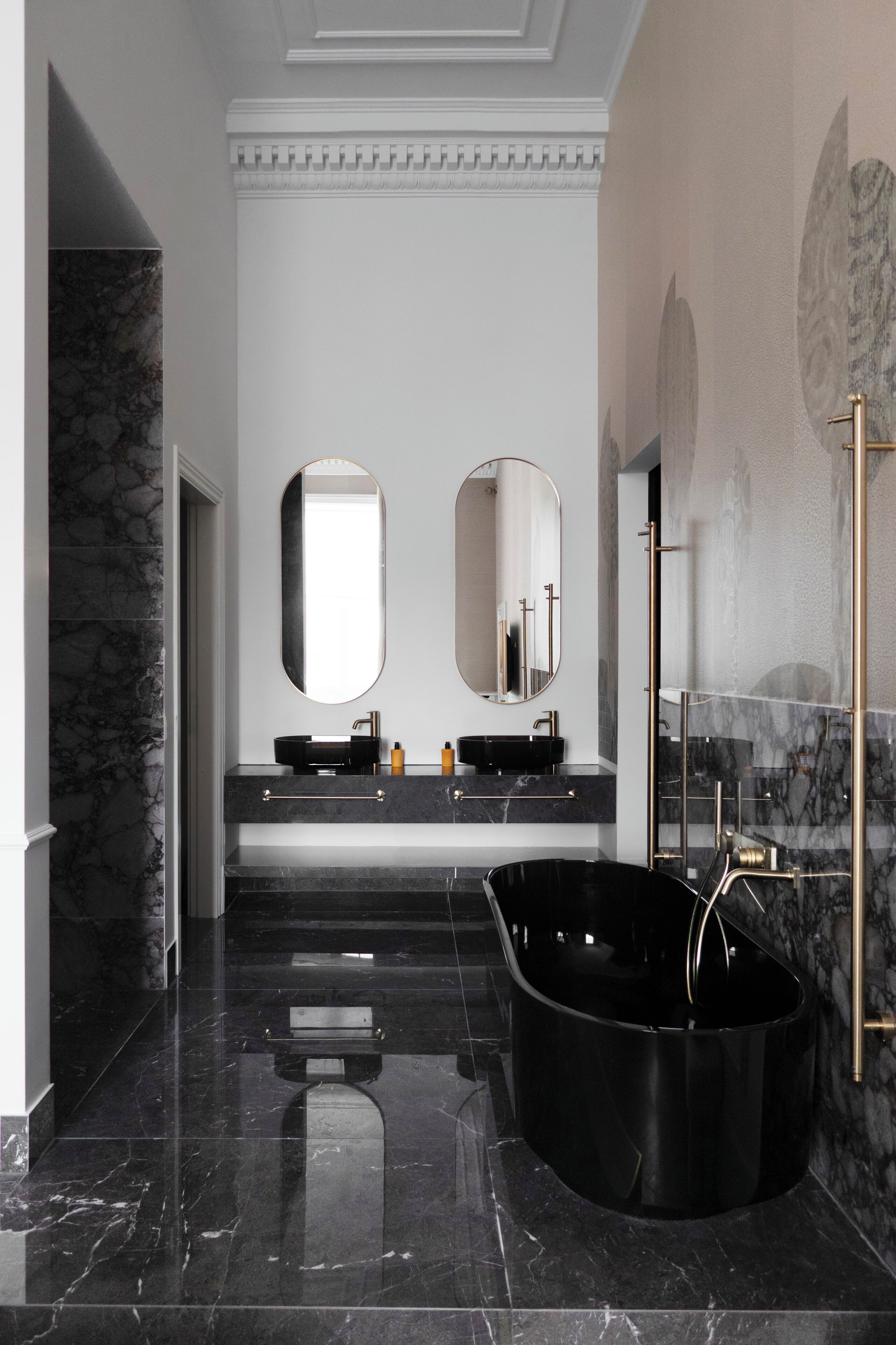 Une salle de bain moderne avec une baignoire noire, deux miroirs ronds et un sol en marbre.