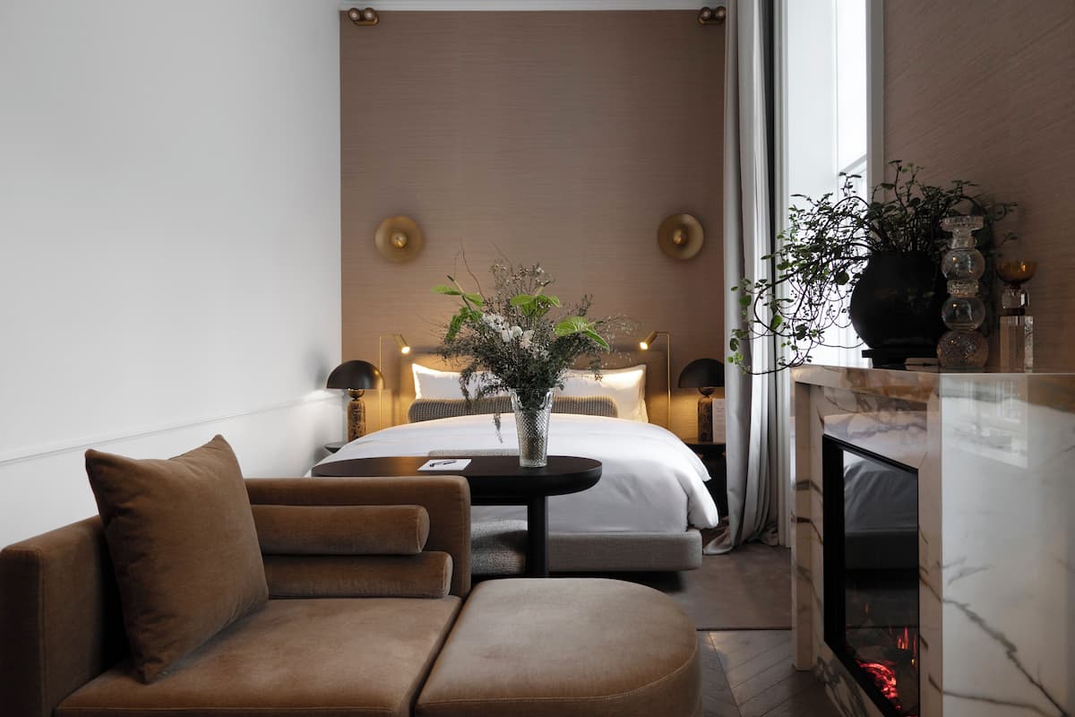 Una habitación de hotel moderna con una cama, un sofá, una mesita y una chimenea.