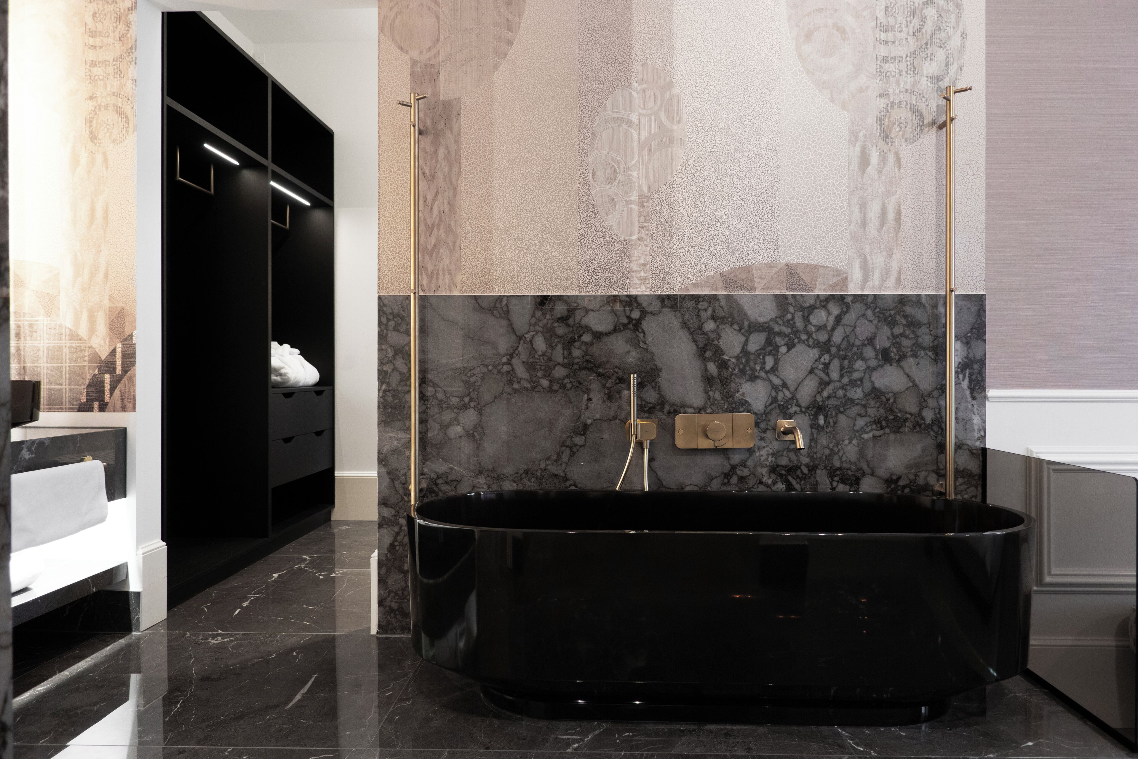 A modern bathroom with a black freestanding bathtub, marble walls, and a black vanity with gold fixtures.