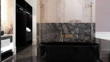 Un baño moderno con una bañera independiente negra, paredes de mármol y un mueble de tocador negro con detalles dorados.