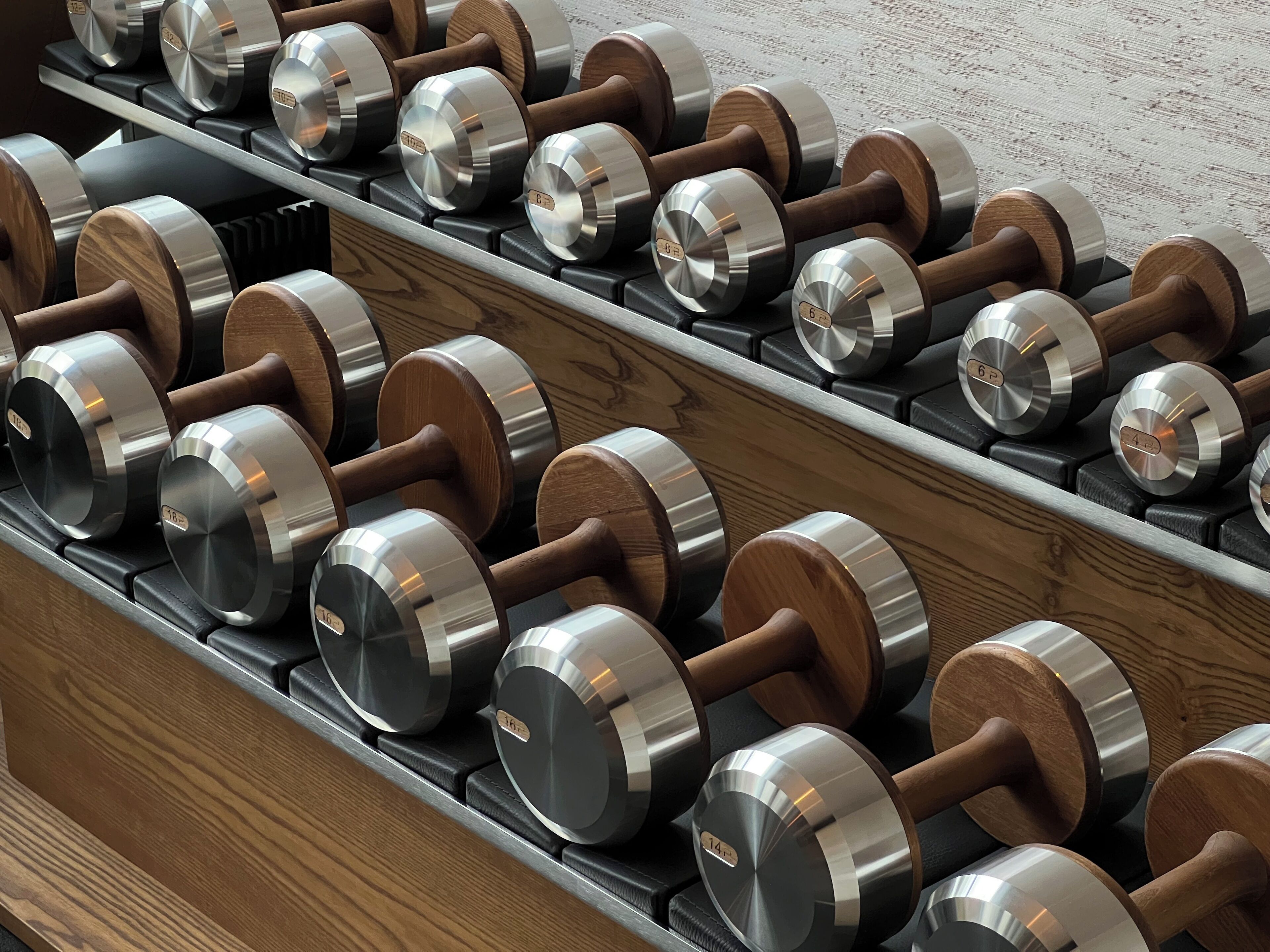 A rack of dumbbells with wooden handles and metallic weights, arranged in rows on a black shelf.