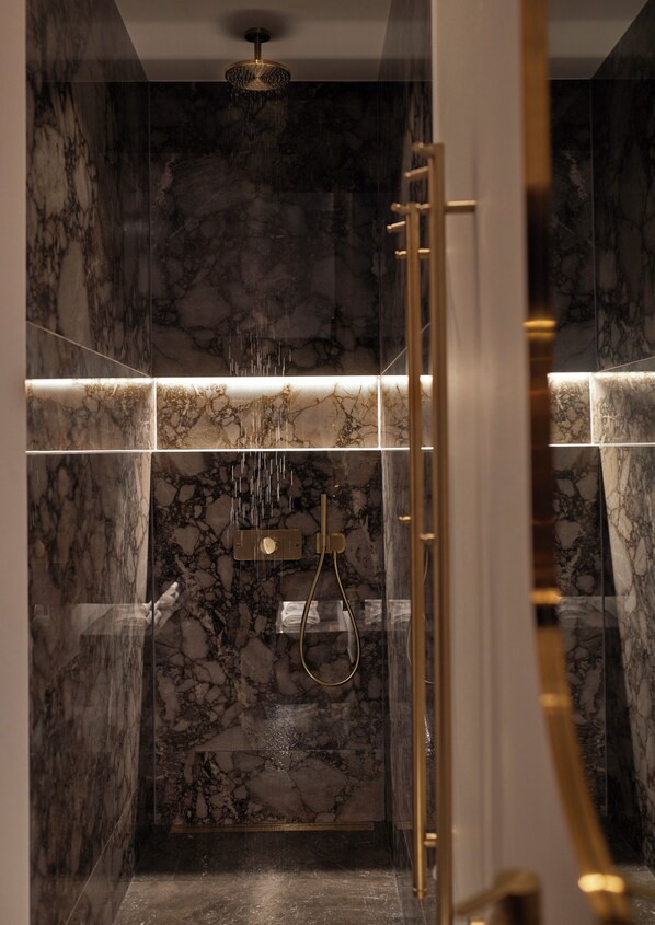 A modern bathroom with marble walls, a glass-enclosed shower, and gold fixtures.