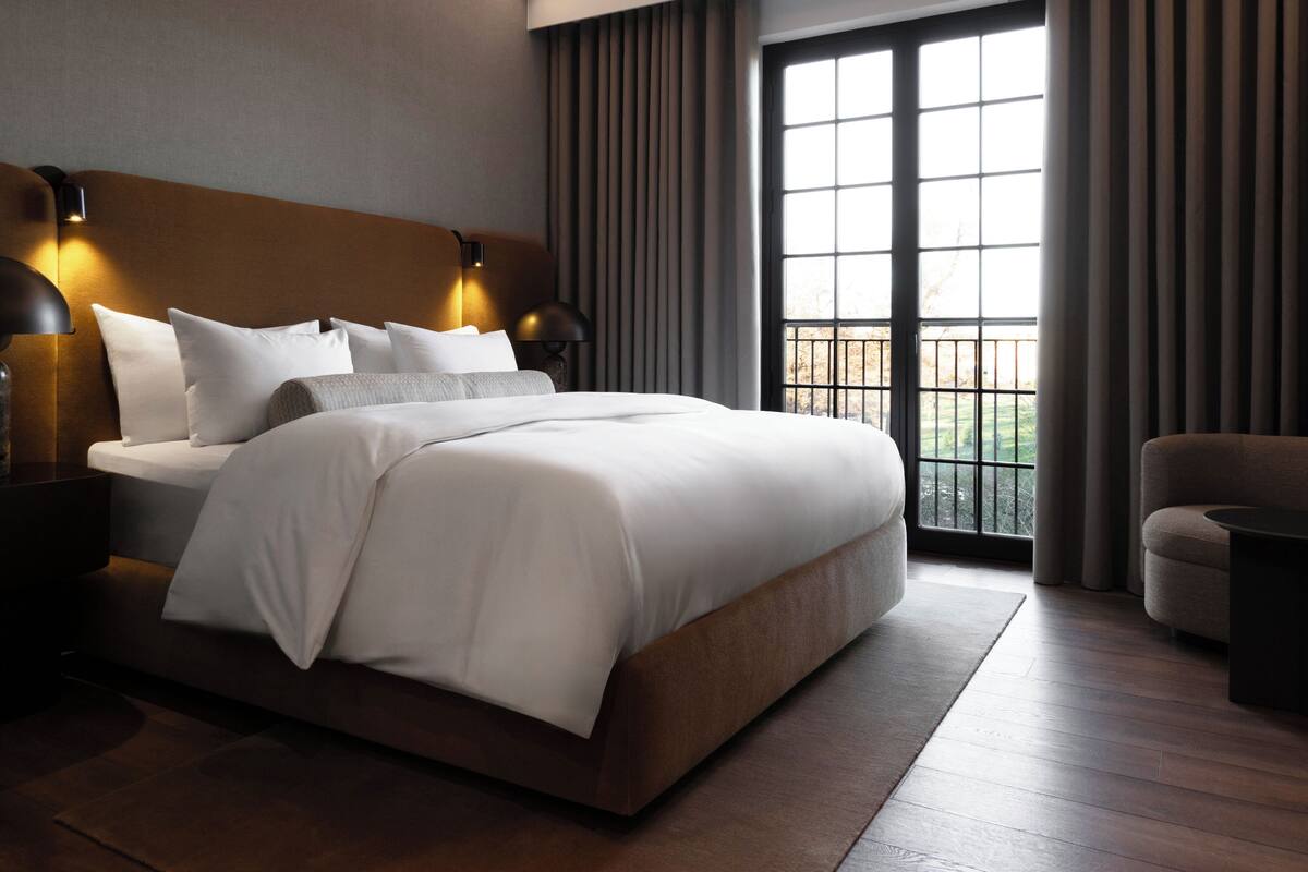 Un cuarto de hotel moderno con una cama grande, dos lámparas de noche, una mesita de noche y vistas al exterior a través de un ventanal amplio.