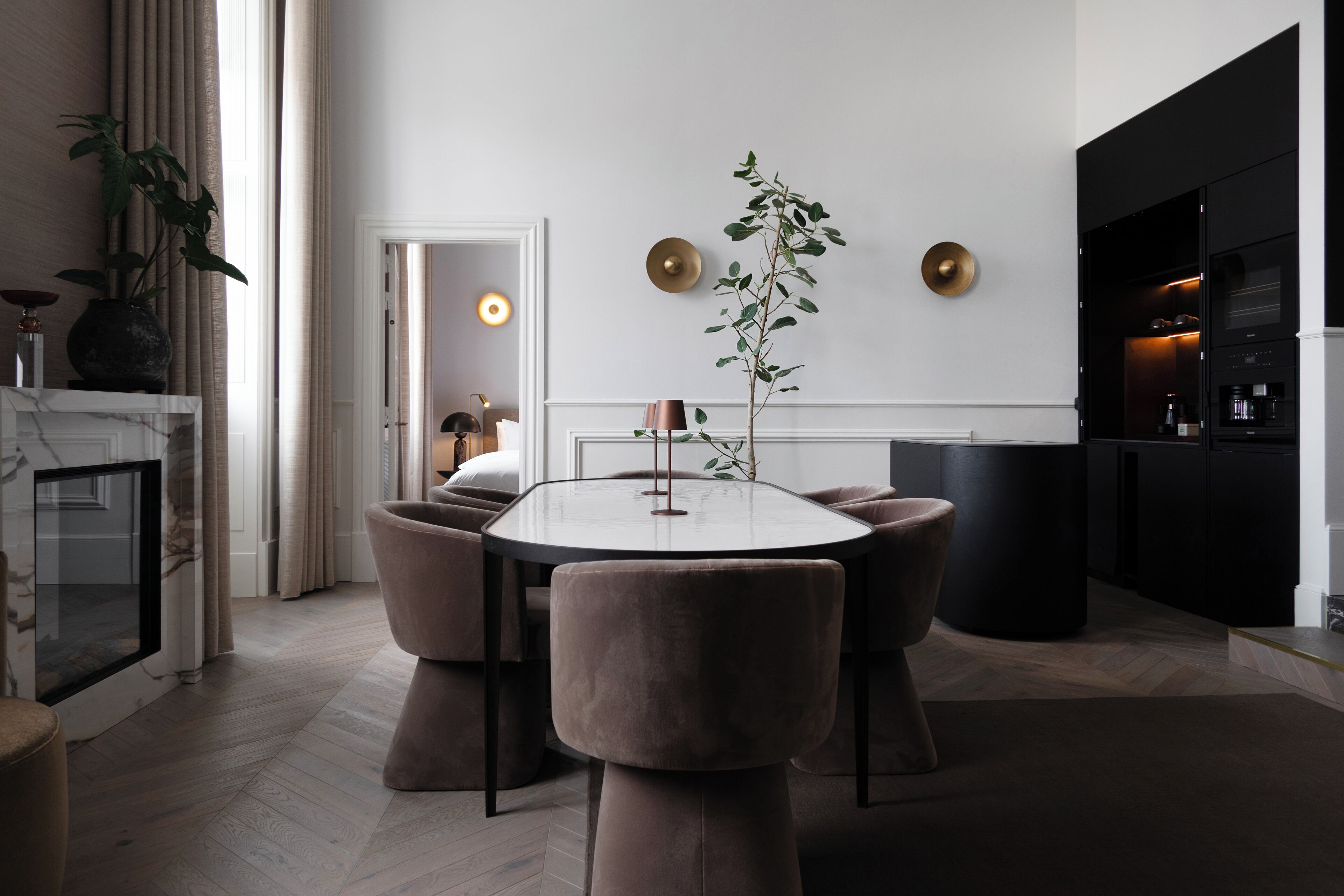 Een moderne eethoek met een ronde tafel, gestoffeerde stoelen en een potplant.