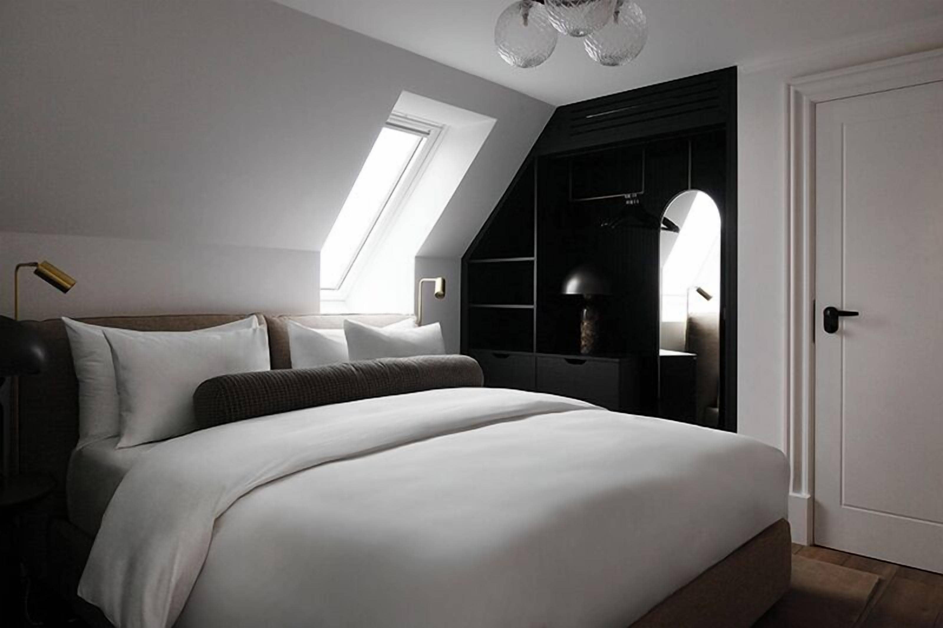 Une chambre moderne avec un grand lit, une fenêtre de toit, un dressing et une porte.