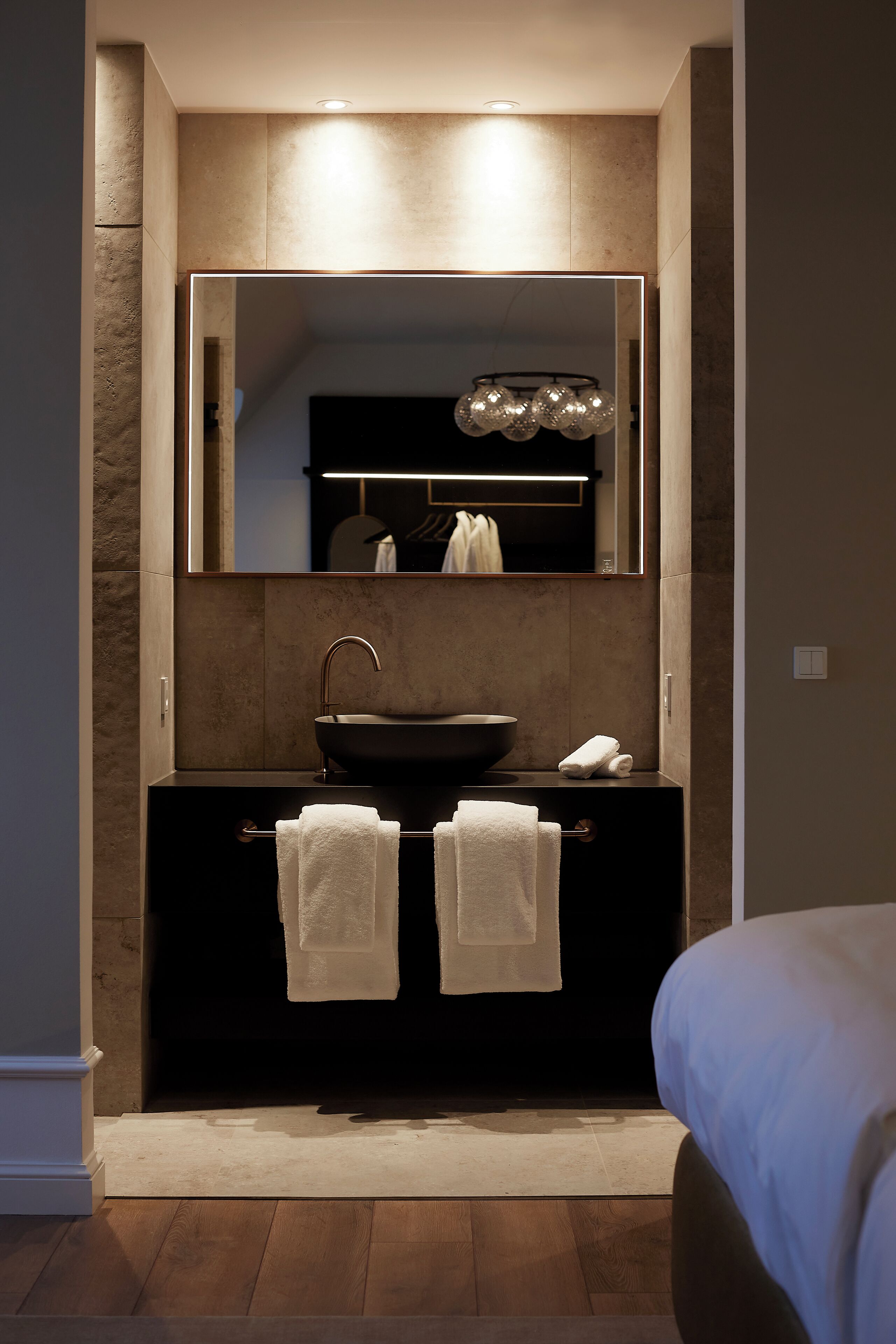 Un bagno moderno con uno specchio grande, un lavandino nero e due asciugamani su un portasciuga.