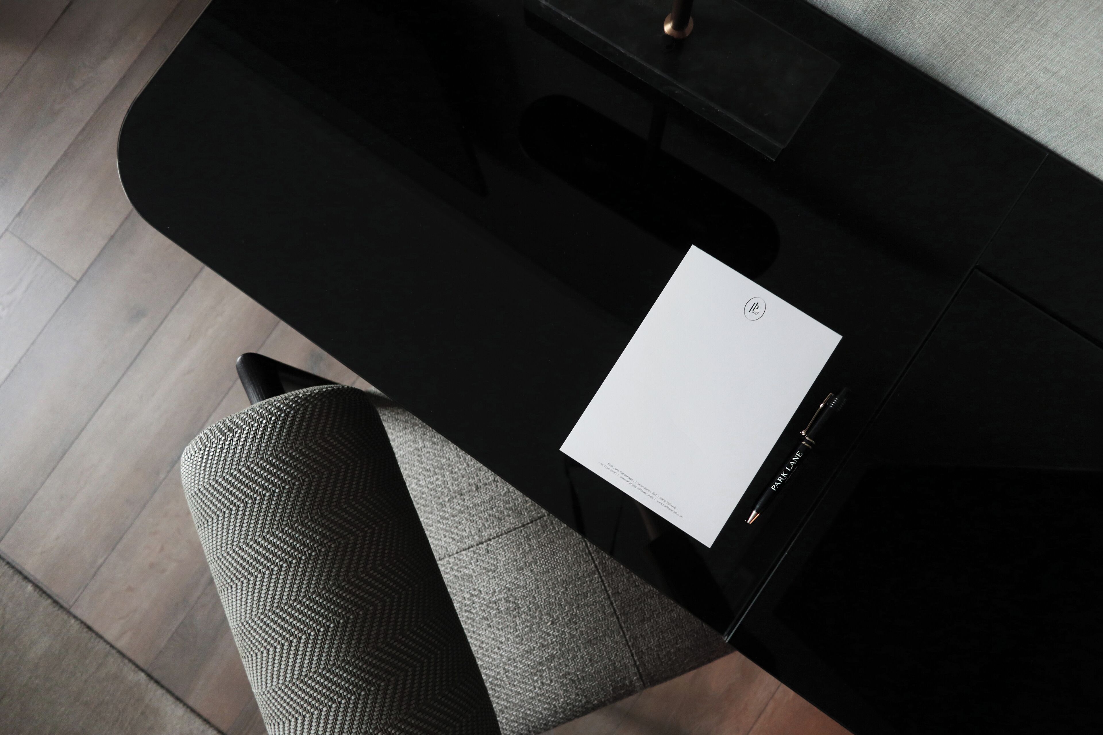 A black table with a white paper on it, a black chair, and a grey patterned cushion.