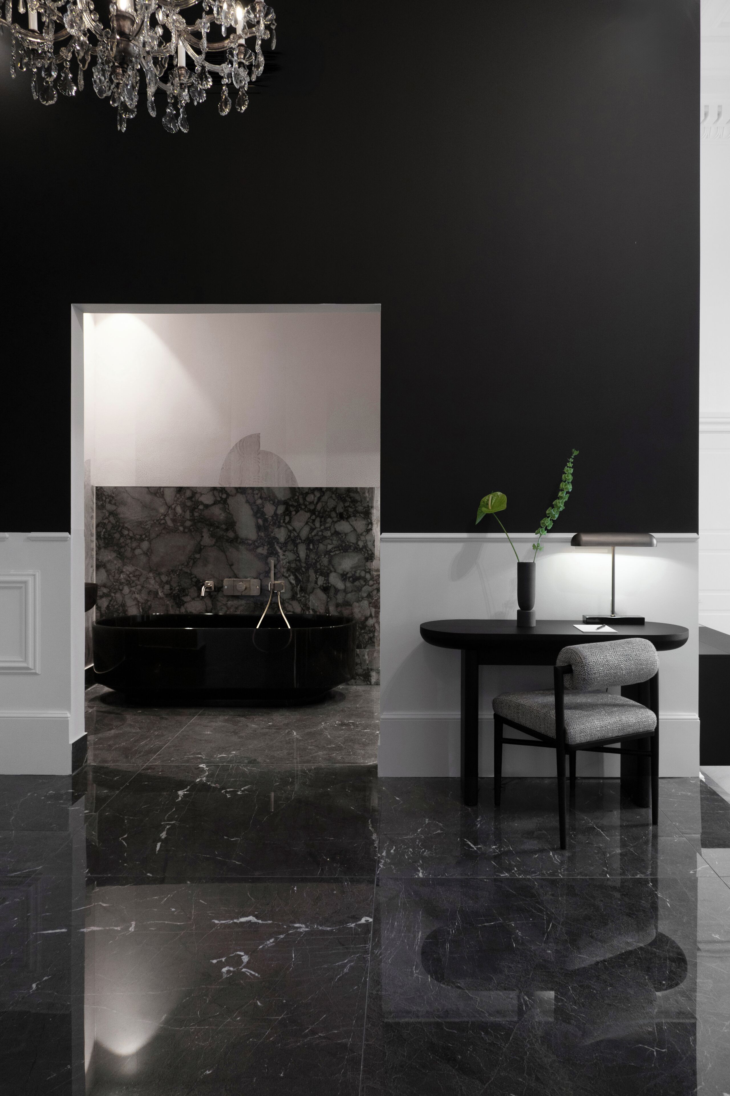 A modern bathroom with a black bathtub, marble wall, and a chandelier.