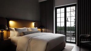 Un dormitorio moderno con una cama grande, una mesita de noche con lámpara, una silla y vistas al exterior a través de un ventanal amplio.