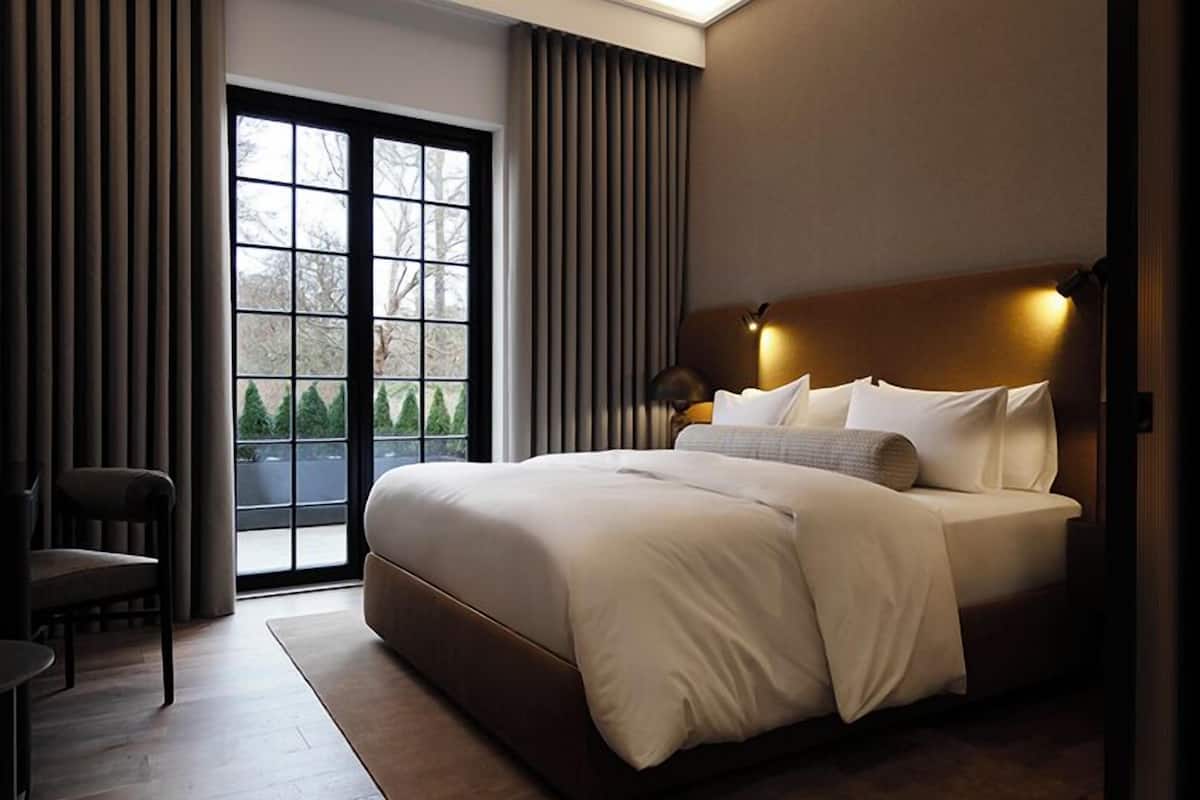 Una habitación de hotel moderna con una cama grande, una silla y vistas al exterior a través de una puerta corredera.