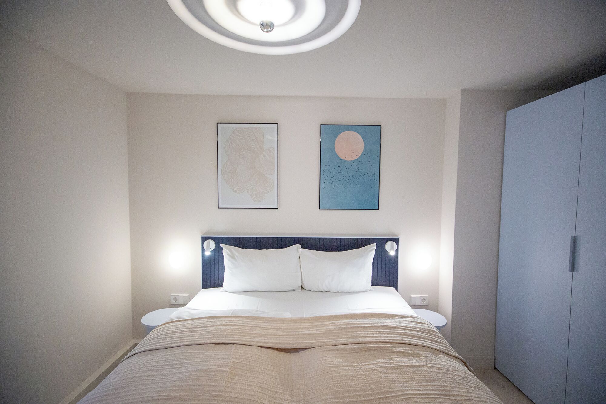 A bedroom with a bed, a nightstand, a wardrobe, and two wall-mounted artworks.