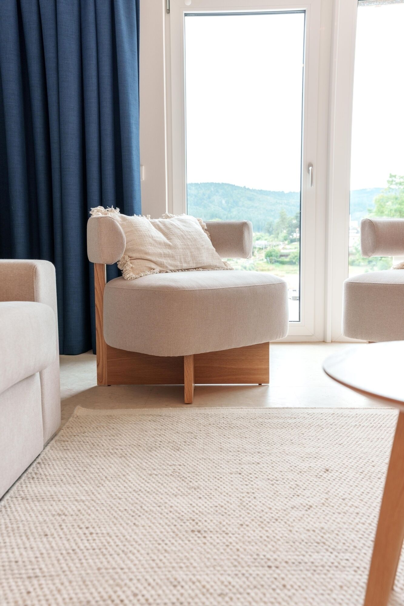 Ein modernes Wohnzimmer mit einer Couch, einem runden Couchtisch und Blick ins Freie durch ein großes Fenster.