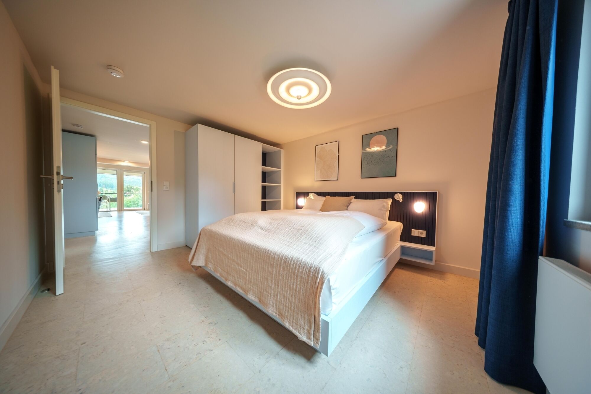 A modern bedroom with a large bed, built-in wardrobe, and a ceiling light fixture.