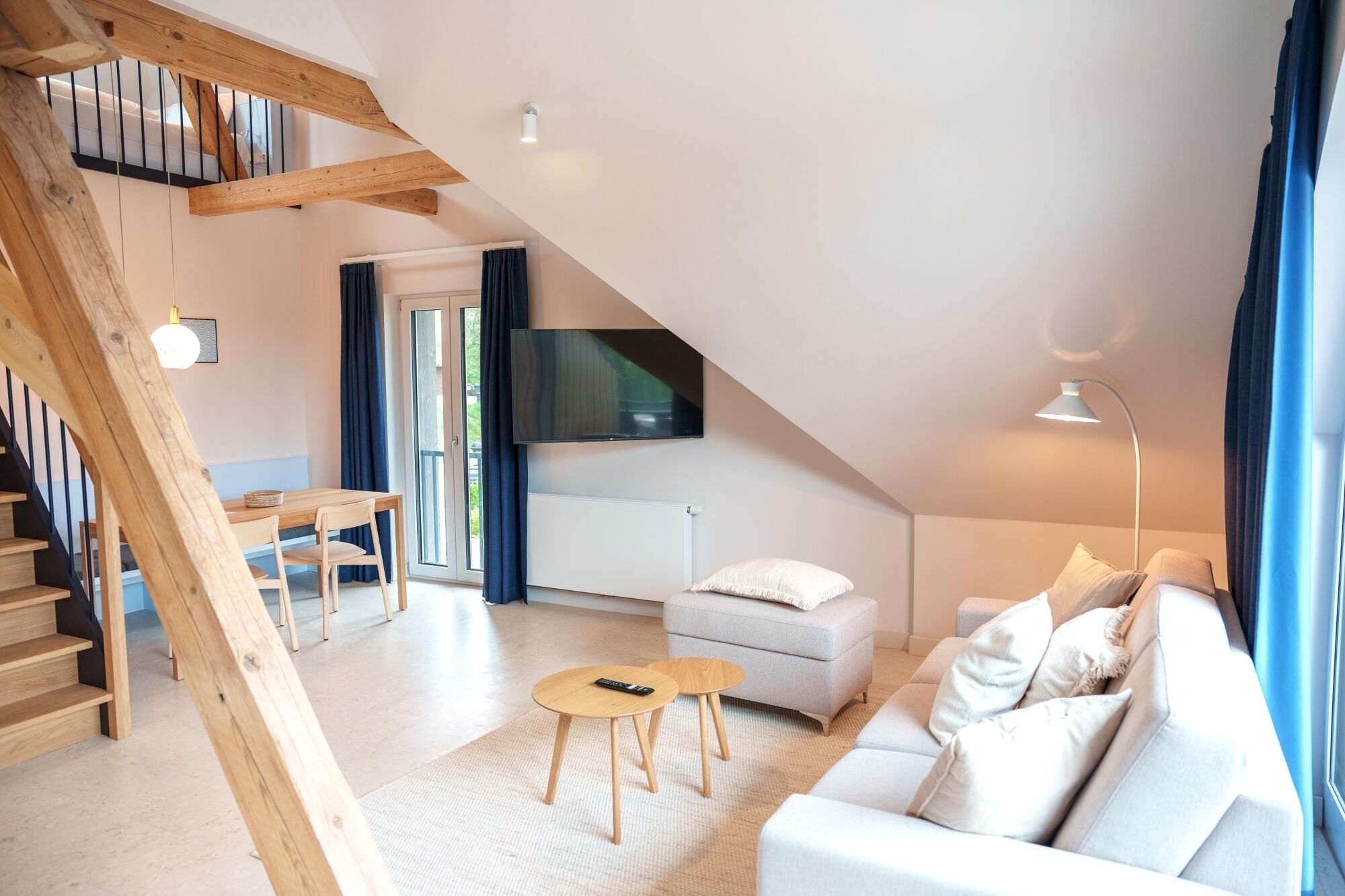 A modern loft-style living space with a staircase, a sofa set, a TV, and a dining area.