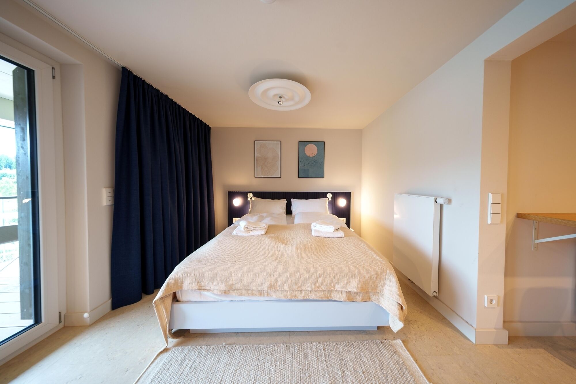Ein modernes Hotelzimmer mit einem großen Bett, einer Deckenleuchte und zwei gerahmten Kunstwerken an der Wand.