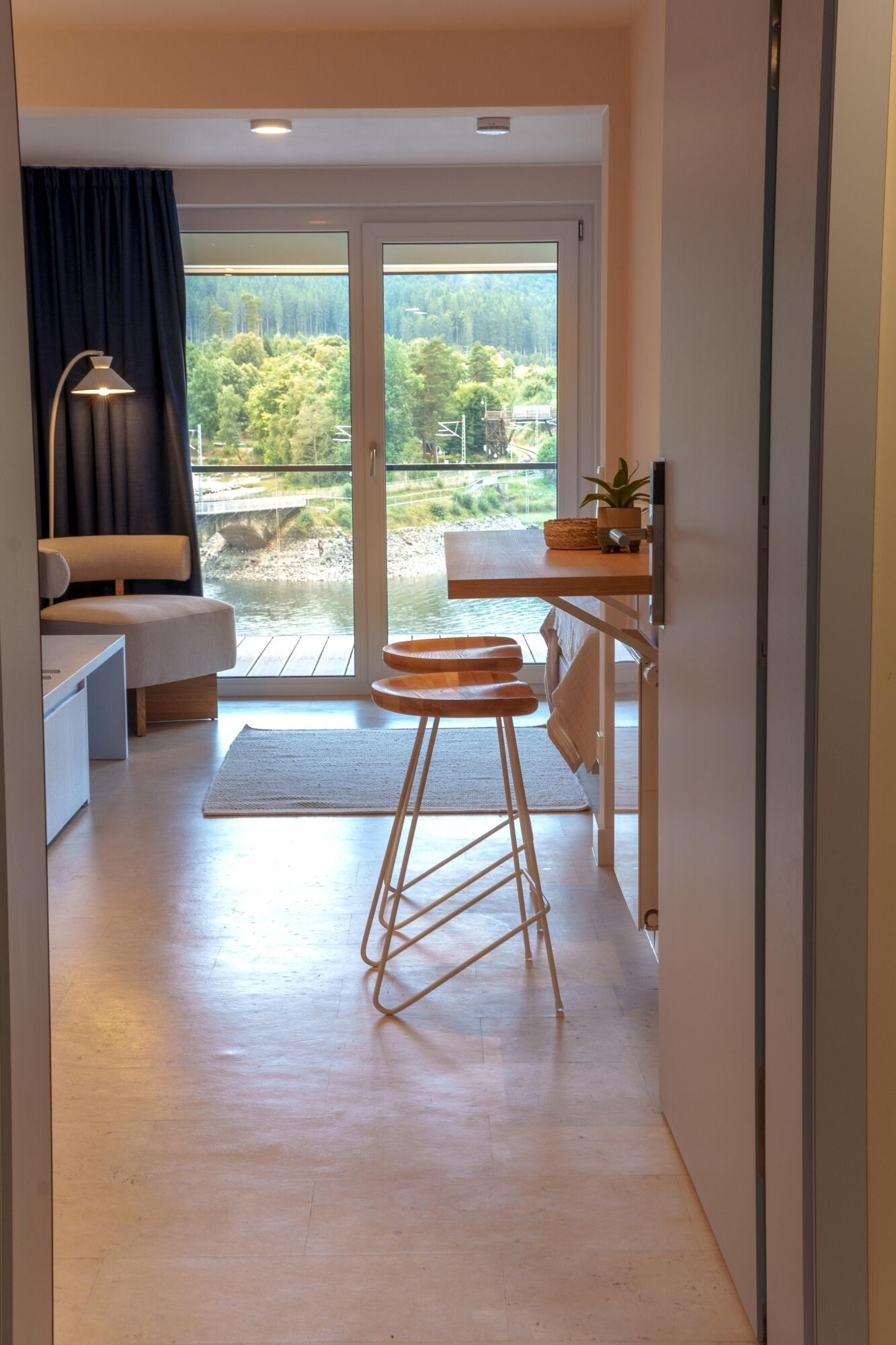 Une cuisine moderne avec un plan de travail en bois, un tabouret et une vue sur un pont et la verdure environnante.