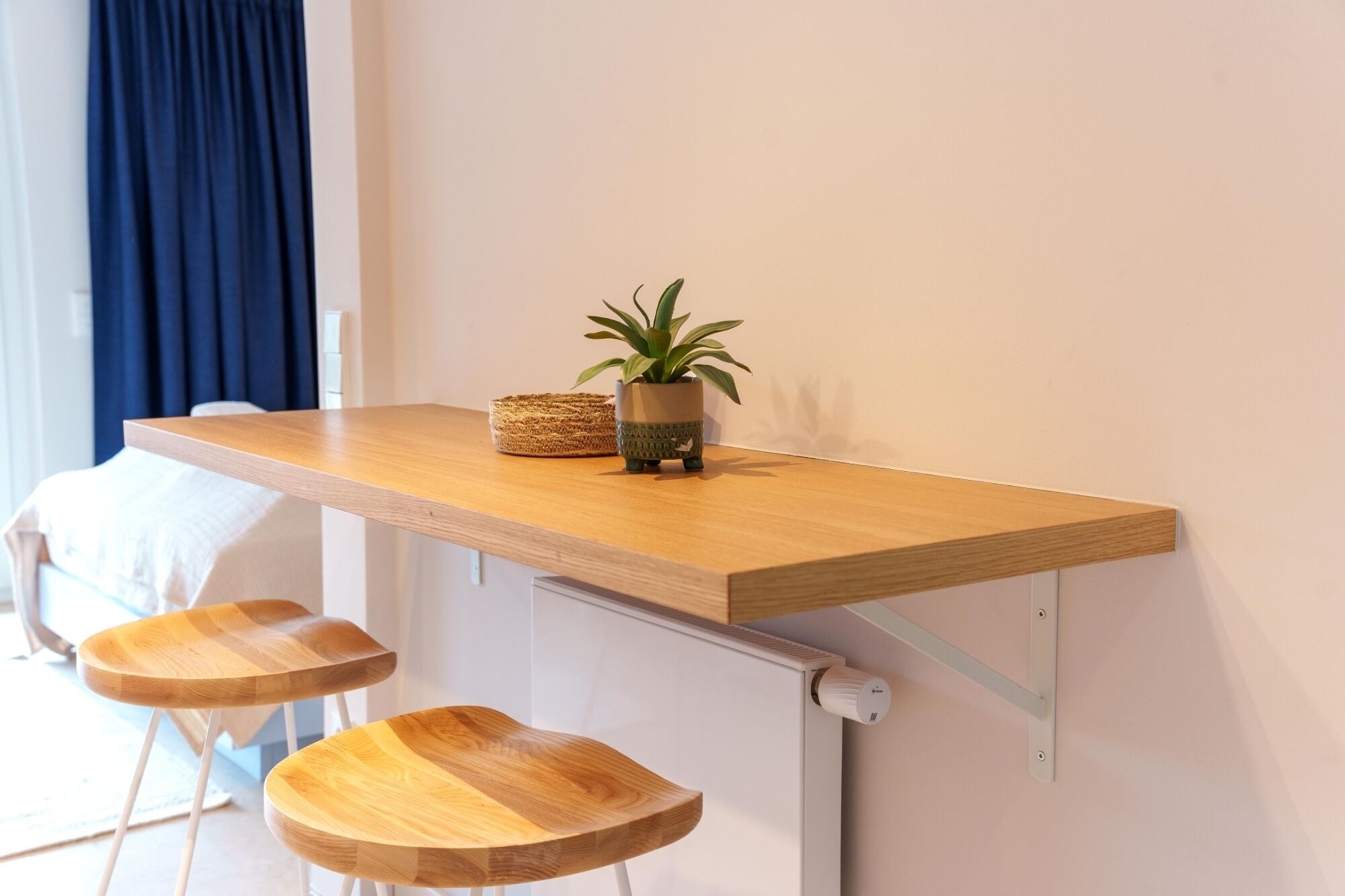 A small wooden table with two stools, a potted plant, and a woven basket.