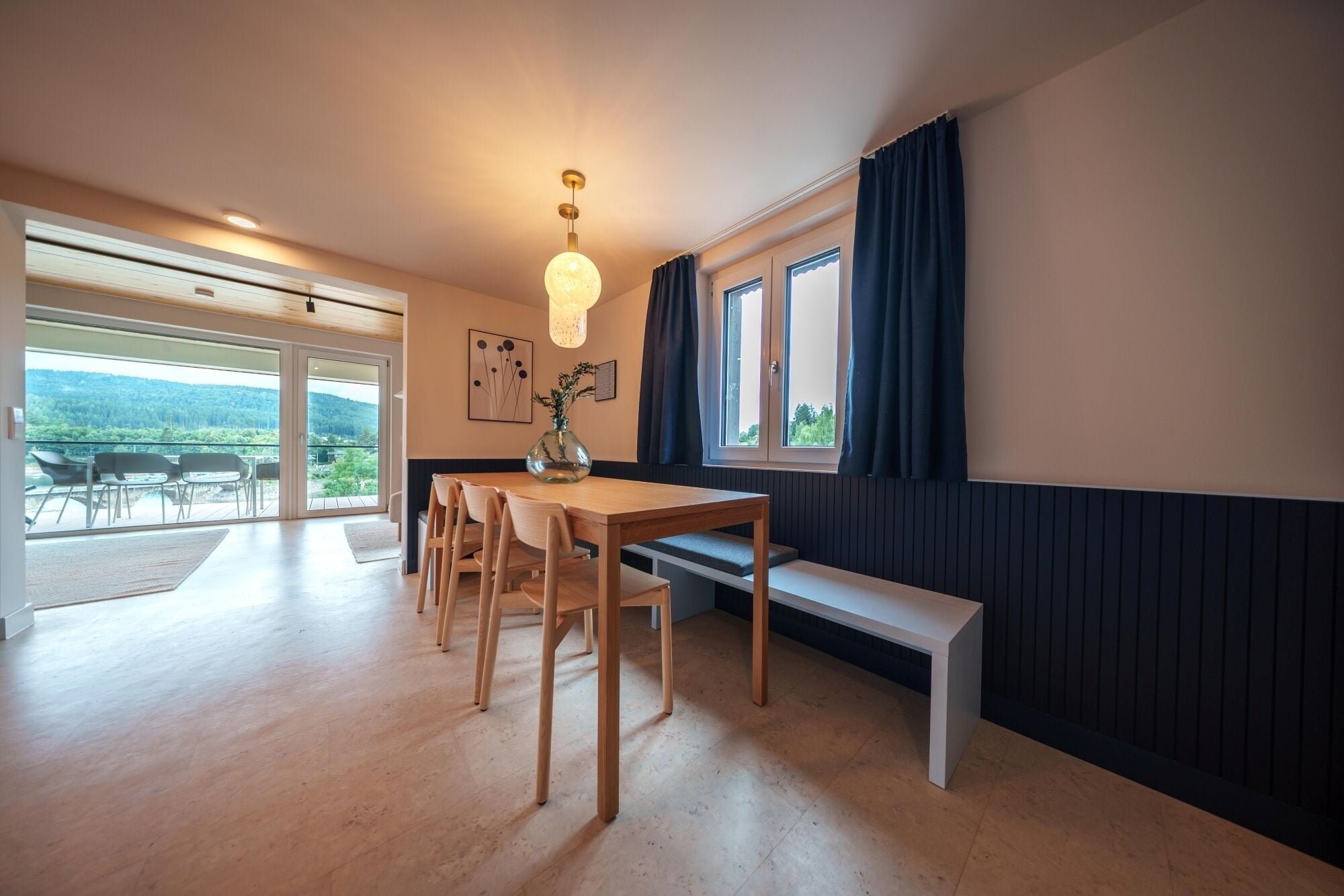 Ein moderner Essbereich mit einem Holztisch, Stühlen und einer Bank, sowie einer Vase mit Blumen.