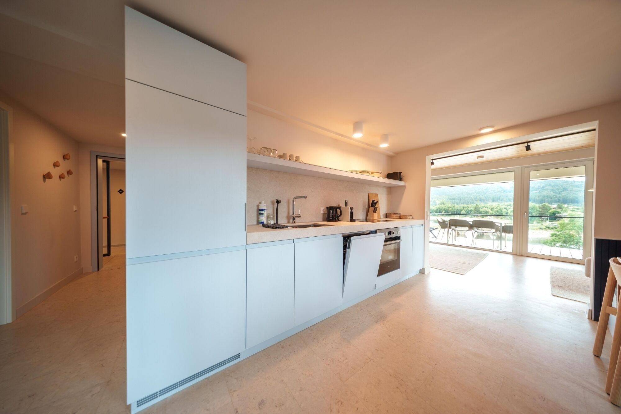 Una cocina moderna con muebles blancos, un horno empotrado y un amplio ventanal con vistas a un paisaje pintoresco.
