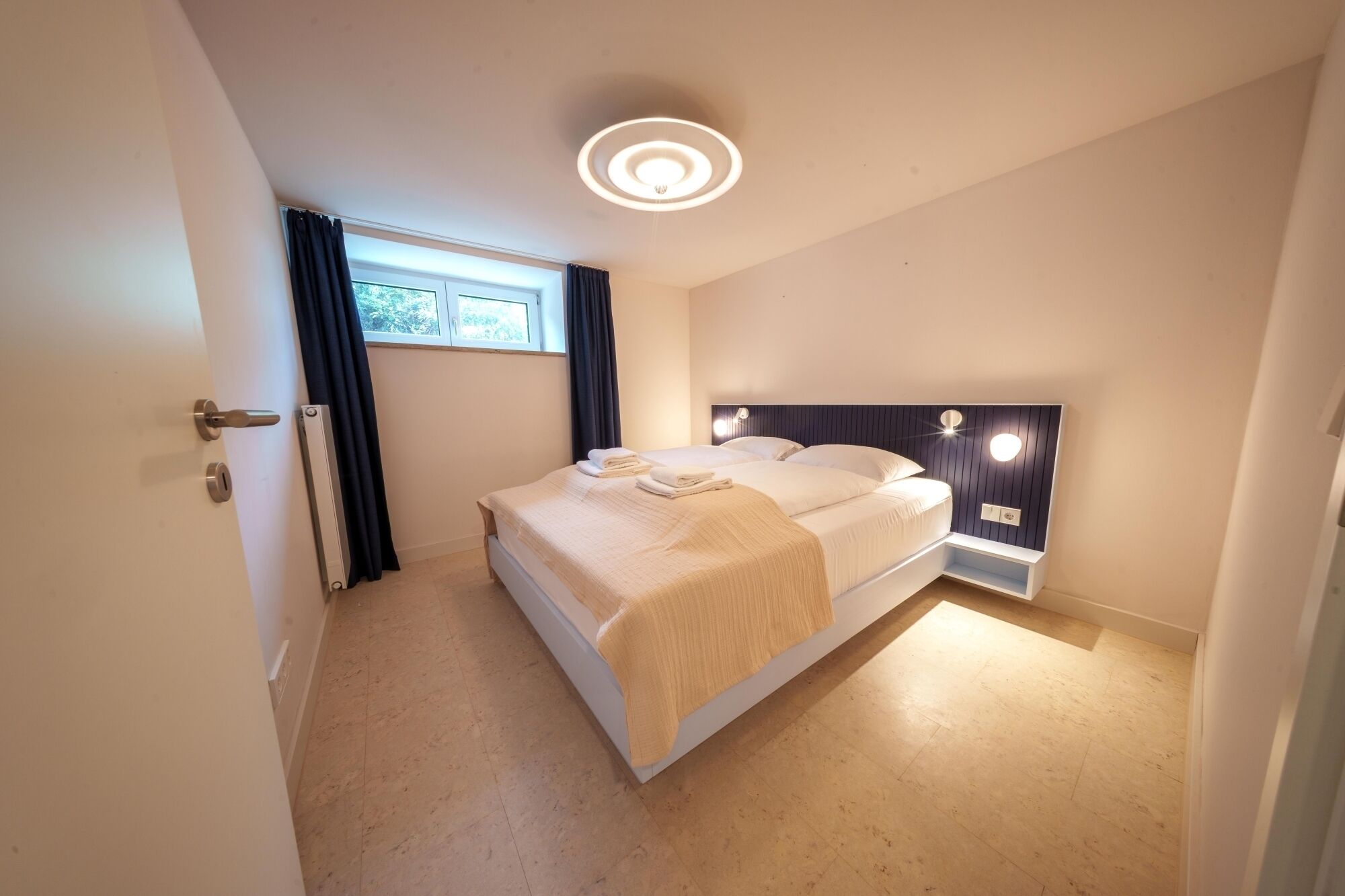 A modern bedroom with a single bed, a built-in nightstand, and a ceiling light fixture.