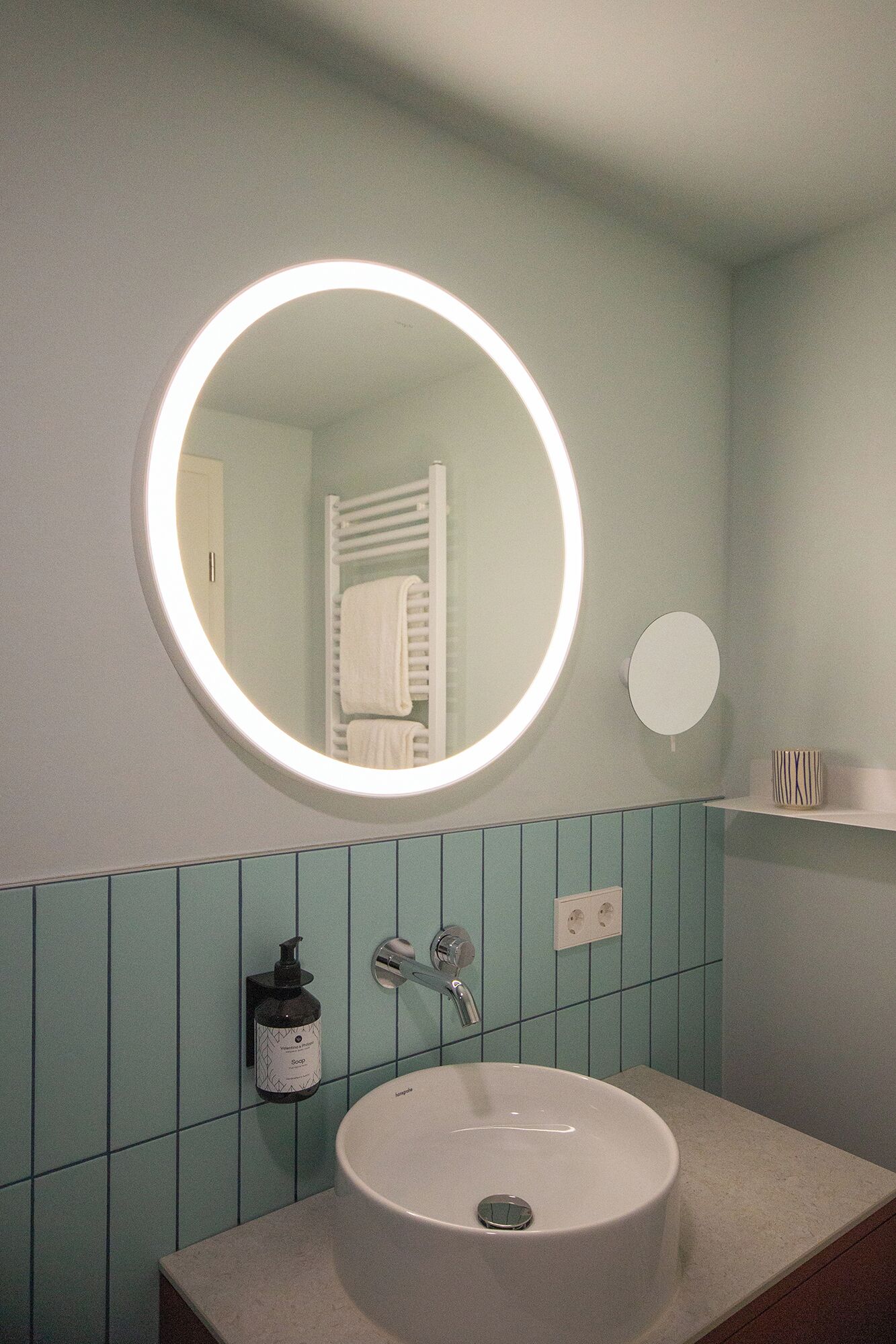 A bathroom with a round mirror, a sink, and a towel rack.