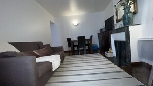 A living room with a sofa, a striped rug, a dining table with chairs, a TV, and a fireplace.