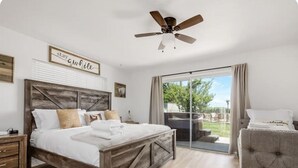 Een slaapkamer met een bed, een plafondventilator, een schuifdeur naar een balkon en een bordje met de tekst 'blijf even'