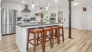 Een moderne keuken met een centraal eiland, roestvrijstalen apparatuur, hangende lampen en houten stoelen.