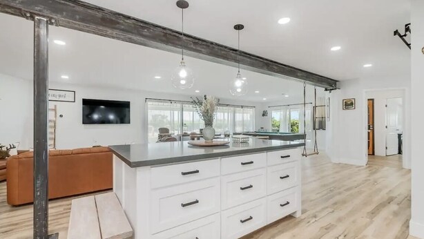 Een moderne keuken met een groot eiland, witte kasten en hangende lampen.