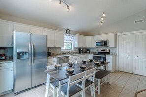 Una cocina moderna con electrodomésticos de acero inoxidable, armarios blancos, una mesa de comedor con sillas y un reloj en la pared.