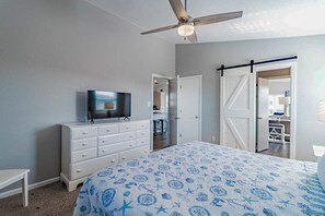 Un dormitorio con una cama, televisión, cómoda y ventilador de techo.