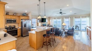 A spacious kitchen with a large island, stainless steel appliances, and wooden cabinets. There is a dining area with a table and chairs, and large windows offering a view of the ocean. - Soundfront serenity with a private dock at Blue Horizon in Salvo! (Salvo)
