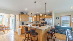 A spacious kitchen with wooden cabinets, a central island with bar stools, stainless steel appliances, and pendant lighting. - Soundfront serenity with a private dock at Blue Horizon in Salvo! (Salvo)