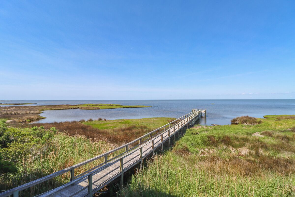 A wooden boardwalk leading to a dock over calm water, surrounded by marshland.
