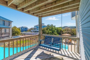 A wooden deck with a bench, a pool, and a view of neighboring houses.