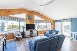 A spacious living room with a large TV, wooden ceiling, and a view of the outside.