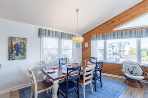 Un coin repas avec une table et des chaises en bois, un luminaire suspendu et une vue sur l’extérieur.
