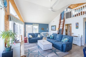 A spacious living room with a high ceiling, a staircase, and a view of the outdoors. - Sunrise views, volleyball court and a quick walk to the beaches by Sun Realty (Duck)
