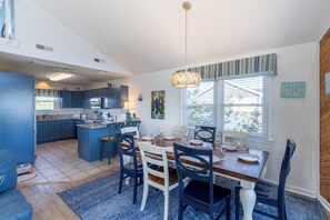 Una cocina moderna con armarios azules, un comedor con mesa y sillas de madera, y un ventanal con persianas.