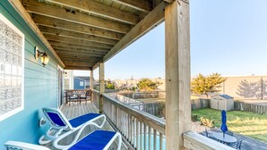 A covered outdoor area with lounge chairs and a table, a wooden deck, and a view of a fenced yard. - Sun Realty ocean and sunrise views from Making Waves in Kill Devil Hills, NC (Kill Devil Hills)