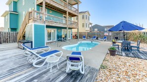 A two-story house with a pool, deck chairs, and a table with umbrellas. - Sun Realty ocean and sunrise views from Making Waves in Kill Devil Hills, NC (Kill Devil Hills)